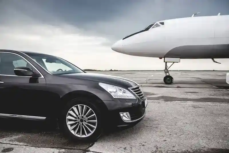 A plane parked on the airport floor with a black Mercedes luxury car in front of it.